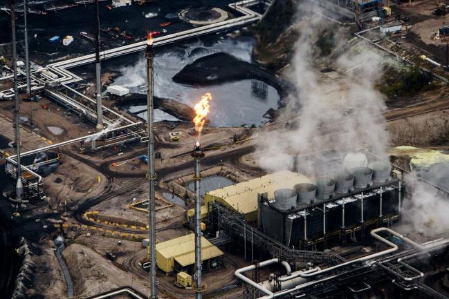 © Bloomberg. Flames shoot from a flare at the Suncor Energy Inc. Millennium upgrader plant in this aerial photograph taken above the Athabasca oil sands near Fort McMurray, Alberta, Canada, on Monday, Sept. 10, 2018. While the upfront spending on a mine tends to be costlier than developing more common oil-sands wells, their decades-long lifespans can make them lucrative in the future for companies willing to wait.