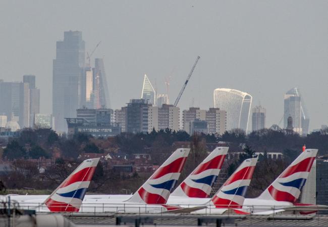 © Bloomberg. The British Airways livery on the tail fins of passenger aircraft at London Heathrow Airport, in view of the skyscrapers in the City of London, U.K., on Wednesday, Feb. 23, 2022. International Consolidated Airlines Group SA, the parent company of British Airways, are due to report results on Friday. Photographer: Chris J. Ratcliffe/Bloomberg