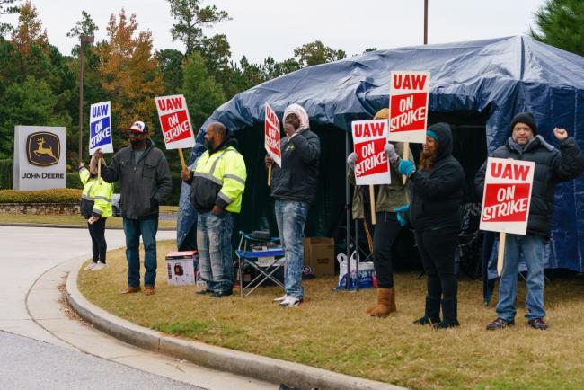 © Bloomberg. Workers hold signs during a strike outside the John Deere Regional Parts Distribution facility in McDonough, Georgia, on Nov. 5.