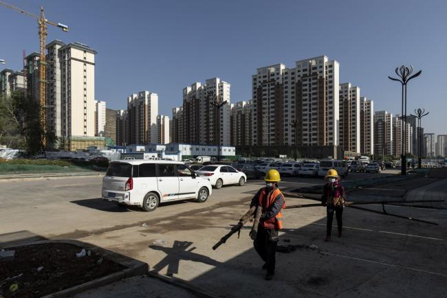 © Bloomberg. Workers carry wooden poles near apartment blocks under construction in the Nanchuan area of Xining, Qinghai province, China, on Tuesday, Sept. 28, 2021. China has urged financial institutions to help local governments stabilize the rapidly cooling housing market and protect the rights of some homebuyers, another signal that authorities are worried about fallout from the debt crisis at China Evergrande Group. Photographer: Qilai Shen/Bloomberg