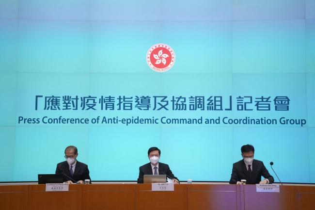 © Bloomberg. Lo Chung-Mau, Hong Kong's secretary for health, from left, John Lee, chief executive, and Sun Dong, secretary for innovation, technology and industry, during a news conference in Hong Kong, China, on Monday, Aug. 8, 2022. Hong Kong will reduce the period of time arrivals must spend in hotel quarantine to three days, plus four days of health monitoring, the latest move to ease travel restrictions that have largely isolated the Asian financial hub throughout the pandemic.