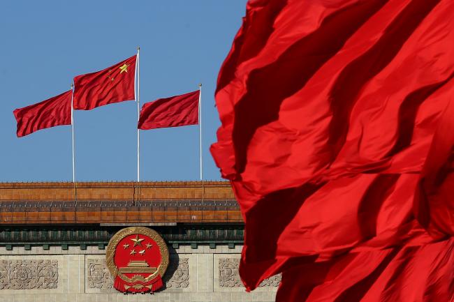 © Bloomberg. BEIJING, CHINA - MARCH 04: Red flags flutter in the wind near the Chinese national emblem outside the Great Hall of the People where sessions of the Chinese People's Political Consultative Conference and National People's Congress are being held on March 4, 2014 in Beijing, China. 
