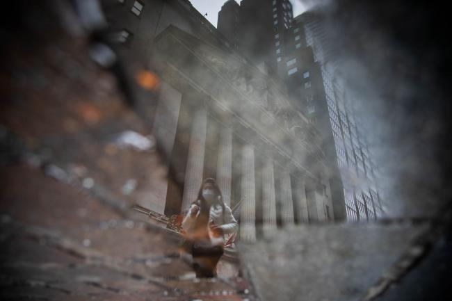 © Bloomberg. A pedestrian reflected in a puddle outside the New York Stock Exchange (NYSE) in New York, U.S., on Friday, Dec. 31, 2021. U.S. stocks swung between gains and losses, with moves exacerbated by thin trading on the last session of the year.