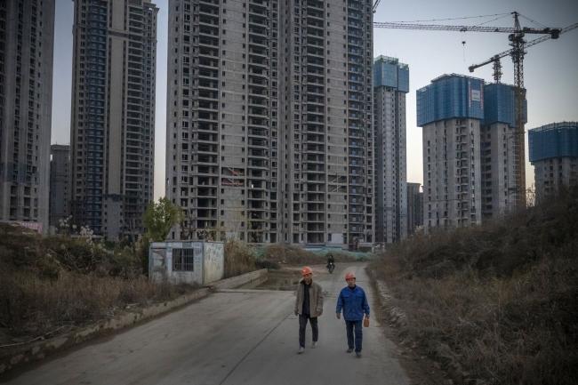 © Bloomberg. Workers walk near unfinished apartment buildings at the construction site of a China Evergrande Group development in Wuhan, China, on Wednesday, Dec. 22, 2021. Defaulter China Evergrande Group is prioritizing payments to migrant workers and suppliers as regulators demand that the developer head off risk of social unrest.