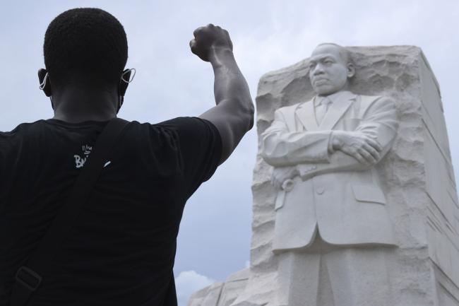 © Bloomberg. WASHINGTON, DC - JUNE 19: A man kneels and raises his fist in the air for eight minutes and 46 seconds -- the time that George Floyd was pinned under a police officer's knee -- during a march and protest to mark the Juneteenth holiday at the Martin Luther King Jr. Memorial June 19, 2020 in Washington, DC. Juneteenth commemorates June 19, 1865, when a Union general read orders in Galveston, Texas stating all enslaved people in Texas were free according to federal law, effectively ending slavery in what remained of the Confederacy. (Photo by Chip Somodevilla/Getty Images) Photographer: Chip Somodevilla/Getty Images North America